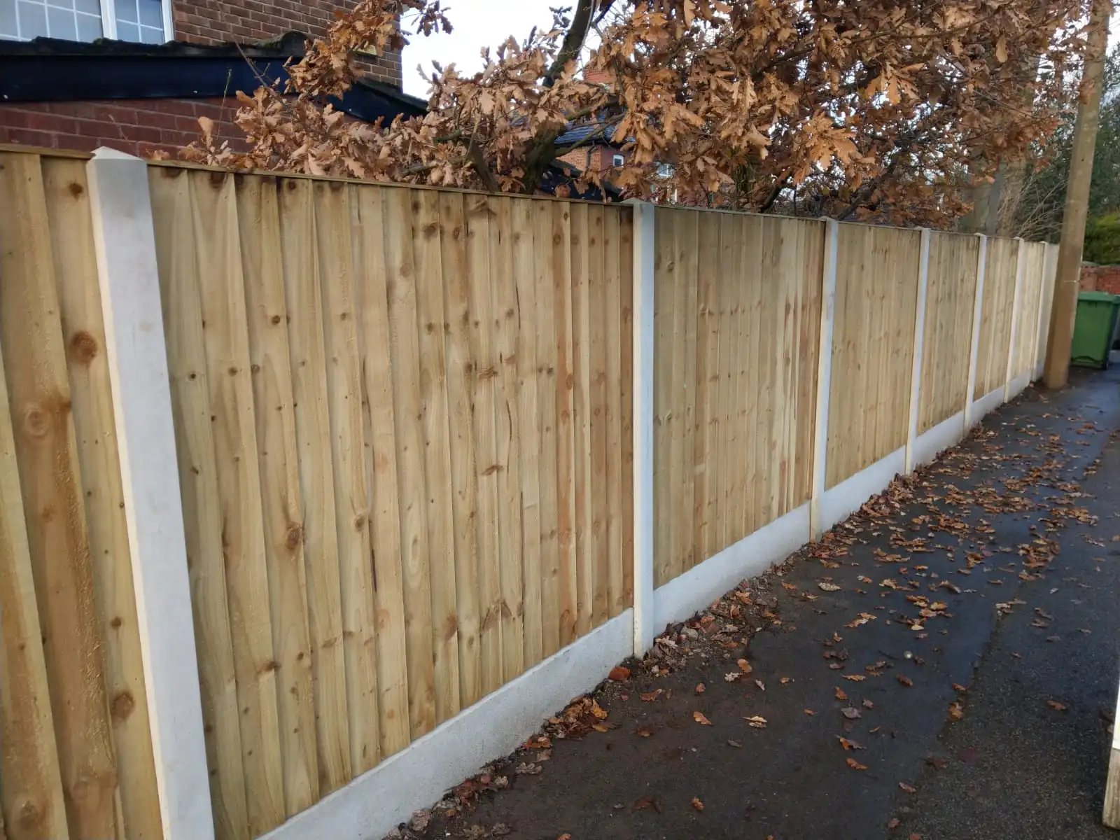 Long run of vertical close-board fencing with concrete gravel boards along driveway
